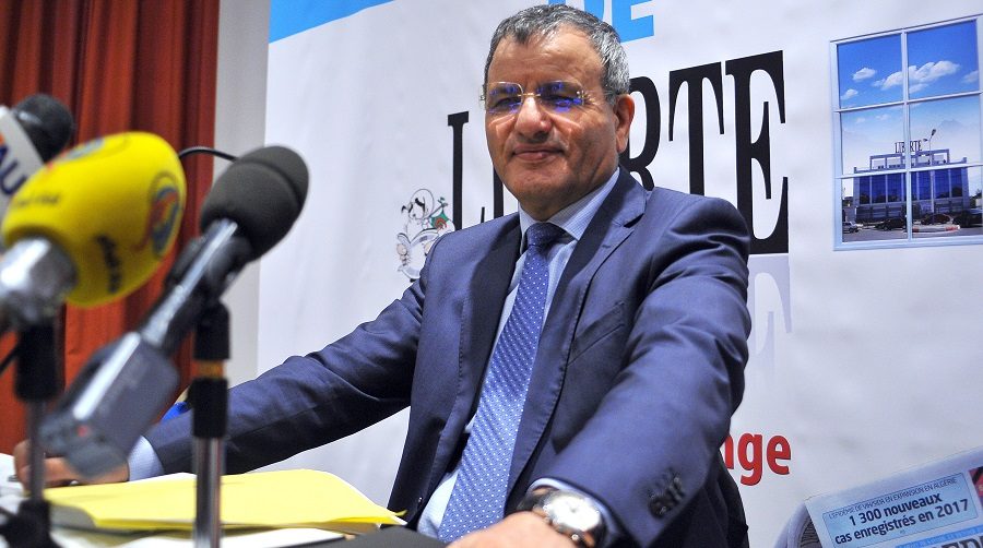 Un homme en costume et lunettes, micros de presse devant lui, lors d'une conférence de presse devant une banderole portant le mot « Liberté ».